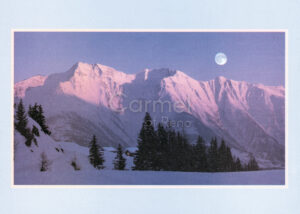 Photo of the moon rising over a snowy mountain range.